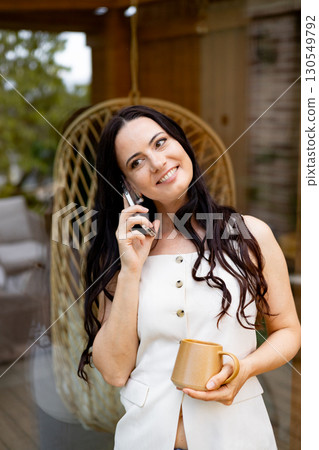 Smiling woman scrolling on smartphone while drinking coffee outdoors. 130549792
