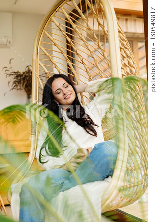 Relaxed woman taking a break, sitting in hanging chair. 130549817