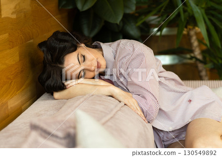 Depressed woman with hair rollers sitting on sofa and thinkiing. 130549892