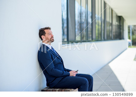 Handsome businessman in suit sitting in front of building and resting. 130549899