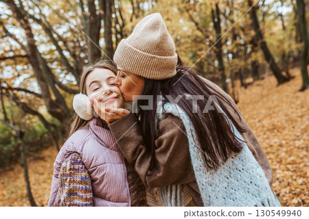 Mother kissing daughter on cheek during walk in autumn nature. 130549940