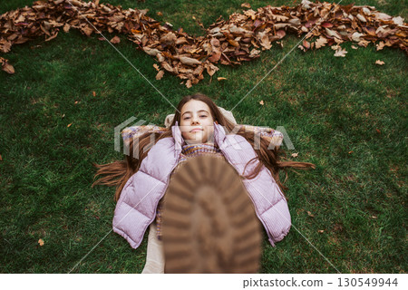Portrait of teen girl laying on grass in the middle of autmn leaves. Portrait of teen girl laying on grass in the middle of autmn leaves. 130549944