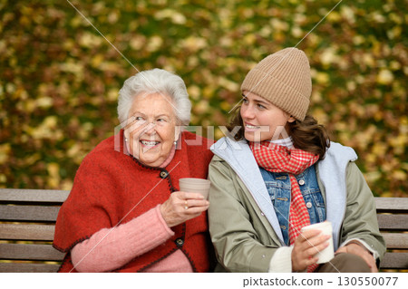 Portrait of a granddaughter and grandmother sitting on bench in autumn park. Portrait of a granddaughter and grandmother sitting on bench in autumn park. 130550077