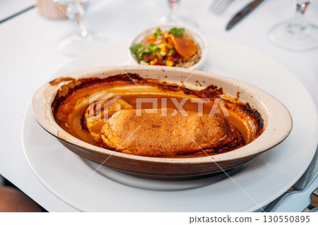Traditional quenelle de brochet in lobster sauce served in an oval ceramic dish on a white tablecloth. Culinary heritage, French cuisine, sustainable fishing, cultural preservation 130550895