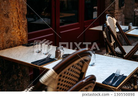 Outdoor cafe tables with marble tops, set with glasses and cutlery in a rustic street setting. Parisian cafe culture, terrace dining, slow living, local hospitality 130550898
