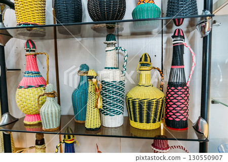 Colorful woven bottles made using traditional techniques displayed on glass shelves. Ethnographic design, traditional weaving techniques, heritage crafts, local craftsmanship Colorful woven bottles made using traditional techniques displayed on glass shelves. Ethnographic design, traditional weaving techniques, heritage crafts, local craftsmanship 130550907