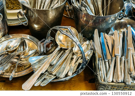 A collection of silver cutlery including knives, forks, and spoons arranged in baskets and trays. Secondhand cutlery, vintage flatware, elegant dining revival, heirloom tableware 130550912