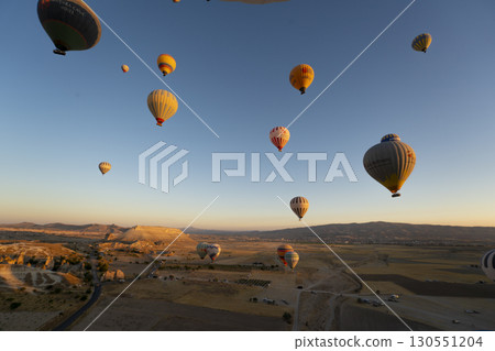 Türkiye Cappadocia: A landscape of strangely shaped mountains and many hot air balloons flying in the sky. 130551204