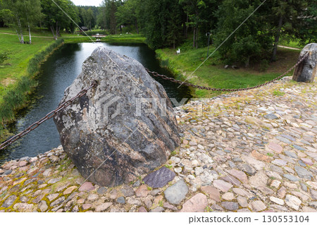 A detailed photograph of a weathered, lichen-covered stone with a metal chain 130553104