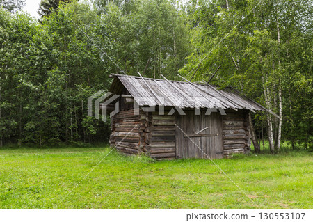A small, weathered wooden cabin surrounded by dense trees 130553107