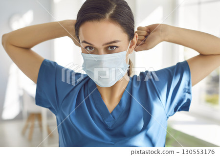 Portrait of young woman doctor wearing medical mask looking at camera in medical clinic. Portrait of young woman doctor wearing medical mask looking at camera in medical clinic. 130553176