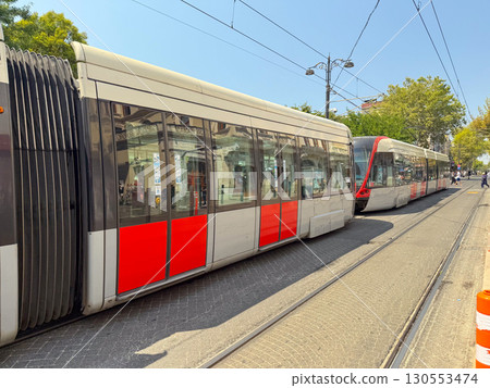 Tram with passengers visible through windows at city station platform. Urban transport, daily commute, and public mobility in modern infrastructure. Tram with passengers visible through windows at city station platform. Urban transport, daily commute, and public mobility in modern infrastructure. 130553474