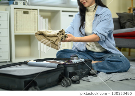 Young woman packing clothes into a suitcase at home while preparing for a trip Young woman packing clothes into a suitcase at home while preparing for a trip 130553490