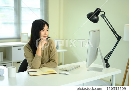 Young woman working at desk with desktop computer, and coffee mug in modern office Young woman working at desk with desktop computer, and coffee mug in modern office 130553509