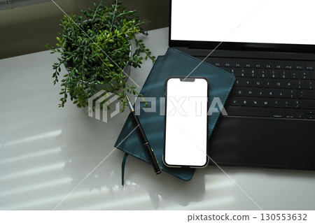 Smartphone with blank screen on notebook, and laptop, with plant decor on desk Smartphone with blank screen on notebook, and laptop, with plant decor on desk 130553632