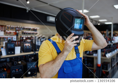 A man in a workwear wearing a protective welding helmet inside a store 130554106