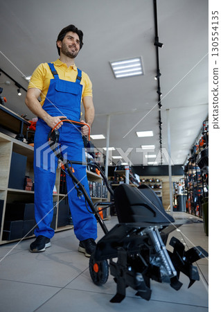A man worker is pushing a lawn mower vigorously A man worker is pushing a lawn mower vigorously 130554135