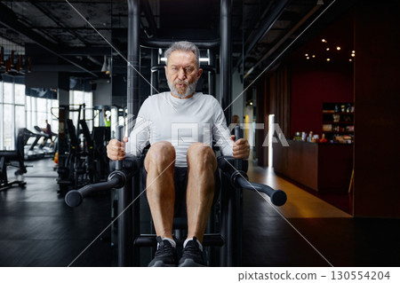 An older gentleman is actively exercising on a machine at a gym 130554204