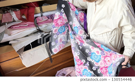 A woman unfolds her yukata in front of a paulownia wood dresser with her kimono spilling out 130554446