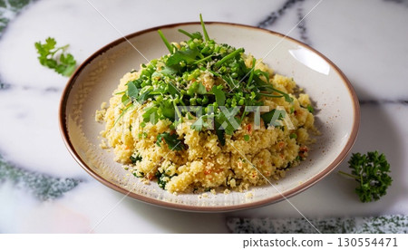 Couscous garnished with greens in a plate on a white marble serving table Couscous garnished with greens in a plate on a white marble serving table 130554471
