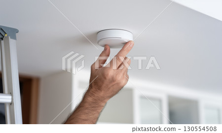 Hand installing smoke detector on ceiling for home safety 130554508