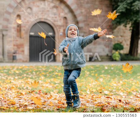 Child in warm clothes enjoying autumn leaves. Playful outdoor moment, carefree fun, healthy childhood 130555563