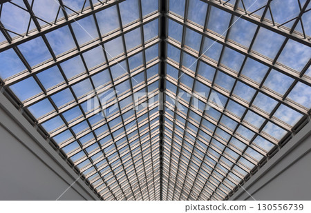 Symmetrical view of a modern glass roof structure with a steel frame, revealing a clear blue sky 130556739