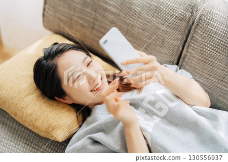 A woman lying on the sofa and using a smartphone A woman lying on the sofa and using a smartphone 130556937