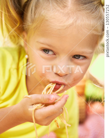 Close up of girl eating spaghetti with messy face at picnic Close up of girl eating spaghetti with messy face at picnic 130557252