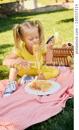 Girl in yellow outfit eating spaghetti during outdoor picnic 130557314