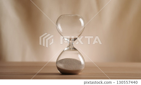 A simple hourglass on a wooden table with a beige backdrop, symbolizing time flow and minimalistic living. Represents timeless themes in a creative, uncluttered presentation for stylish concepts. A simple hourglass on a wooden table with a beige backdrop, symbolizing time flow and minimalistic living. Represents timeless themes in a creative, uncluttered presentation for stylish concepts. 130557440