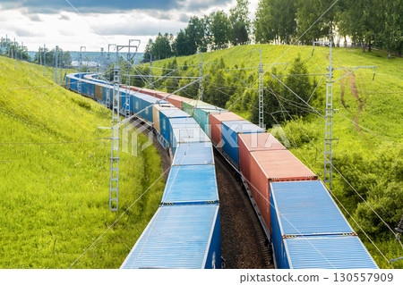 Railway container transportation . Two freight trains with containers are traveling in parallel among green hills in nature in a beautiful place. 130557909