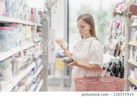 Woman shops for cosmetics and household items while carefully examining product labels in supermarket aisle 130557914