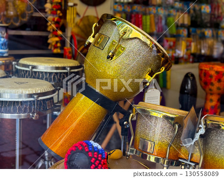 Shiny golden percussion drum displayed in a music shop among traditional instruments. Cultural rhythm, artistic heritage, and musical craftsmanship expressed in design. 130558089