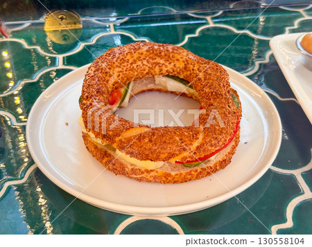 Traditional Turkish simit with sesame seeds filled with cheese, tomato, and cucumber. Street food, culinary heritage, and cultural symbol of savory bakery cuisine. 130558104