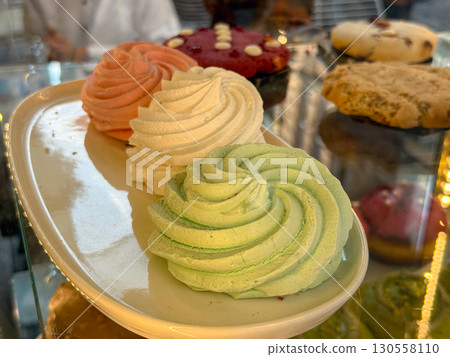 Colorful marshmallow swirls arranged on a white plate in a bakery display. Sweet confectionery, artisan dessert, and fluffy handmade treat symbolizing indulgence. 130558110