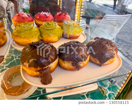 Chocolate-covered donuts with creamy filling displayed on a plate in a bakery shop. Sweet indulgence, gourmet dessert and confectionery temptation capturing flavor and delight. 130558115