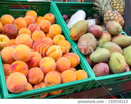 Fresh peaches and mangoes arranged in green crates at a market stall. Seasonal produce, agricultural harvest, and tropical fruit trade reflecting natural abundance. 130558123