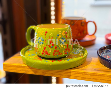 Bright green ceramic cup with floral ornament placed on matching saucer in a shop. Handcrafted artisan design, decorative tradition, and cultural craft symbolism. Bright green ceramic cup with floral ornament placed on matching saucer in a shop. Handcrafted artisan design, decorative tradition, and cultural craft symbolism. 130558133
