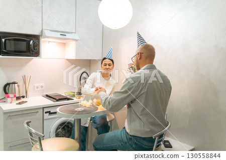Couple Birthday Kitchen Celebration: Happy couple celebrates birthday in small apartment kitchen, enjoying intimate moment. Couple Birthday Kitchen Celebration: Happy couple celebrates birthday in small apartment kitchen, enjoying intimate moment. 130558844