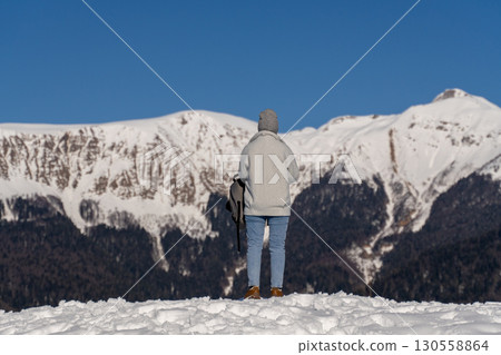 Snow Mountains Person Winter: Solo hiker admires snow-capped mountain range, sunny day, scenic vista. 130558864