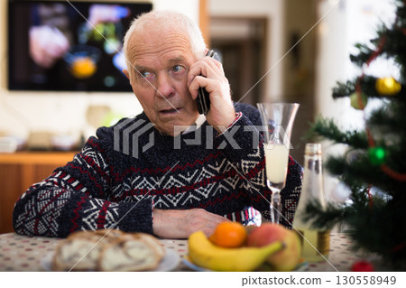 Upset older man talking on phone at table during New Year celebration 130558949