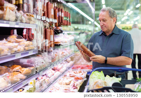 Elderly man chooses sausage in supermarket 130558950