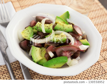 salad of black tomatoes, avocado and onions in white ceramic bowl 130558952