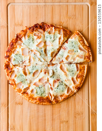 Sliced pizza with visible pieces and toppings on wooden board. Sharing, leisure and culinary enjoyment in everyday dining. Sliced pizza with visible pieces and toppings on wooden board. Sharing, leisure and culinary enjoyment in everyday dining. 130559615