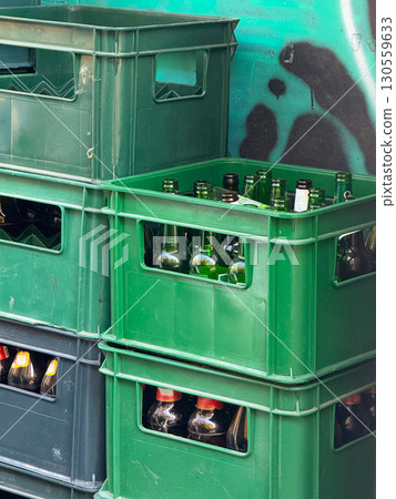 Green plastic crates with empty glass bottles on street corner. Recycling, sustainability and urban consumption in modern lifestyle. Green plastic crates with empty glass bottles on street corner. Recycling, sustainability and urban consumption in modern lifestyle. 130559633