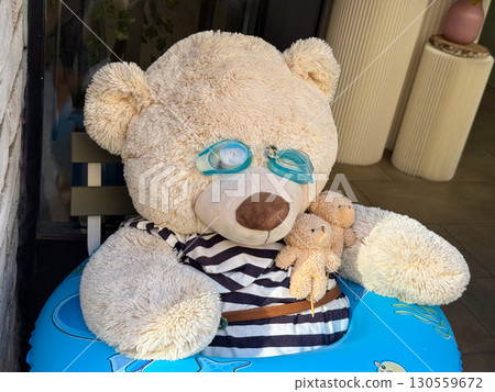 Funny large teddy bear with goggles, striped shirt and inflatable ring. Whimsy, childhood joy and playful decoration in urban setting. Funny large teddy bear with goggles, striped shirt and inflatable ring. Whimsy, childhood joy and playful decoration in urban setting. 130559672