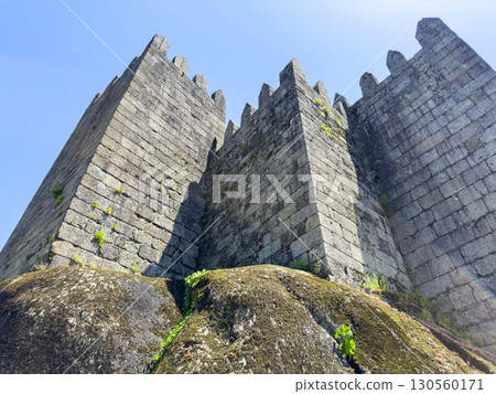 Bottom view of Guimaraes Castle stone towers in Portugal against a clear blue sky. The medieval 130560171