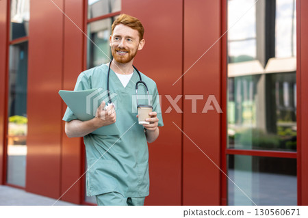 Man doctor with beard walking in scrubs holding coffee and folder Man doctor with beard walking in scrubs holding coffee and folder 130560671