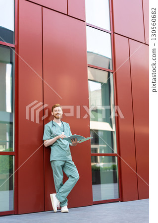 Man doctor studying papers in open medical chart near hospital building 130560682